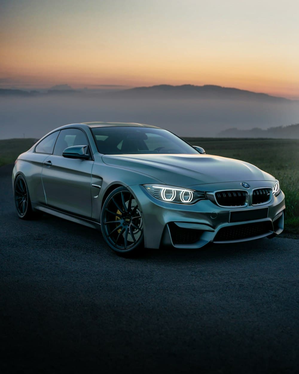 Silver coupe parked on a quiet road at dawn, headlights on in the mist