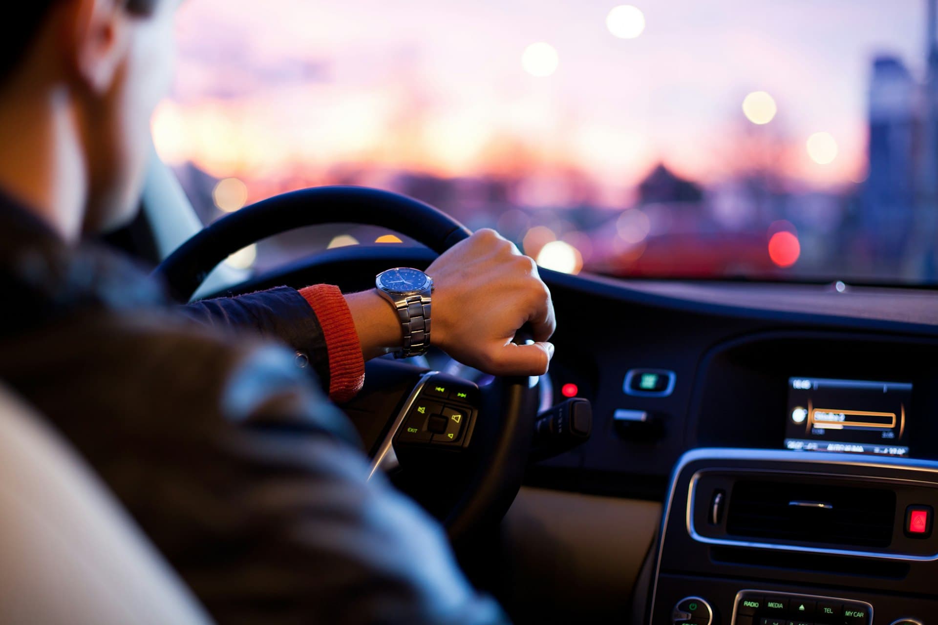 Driver at the wheel at dusk, city lights blurred through the windscreen